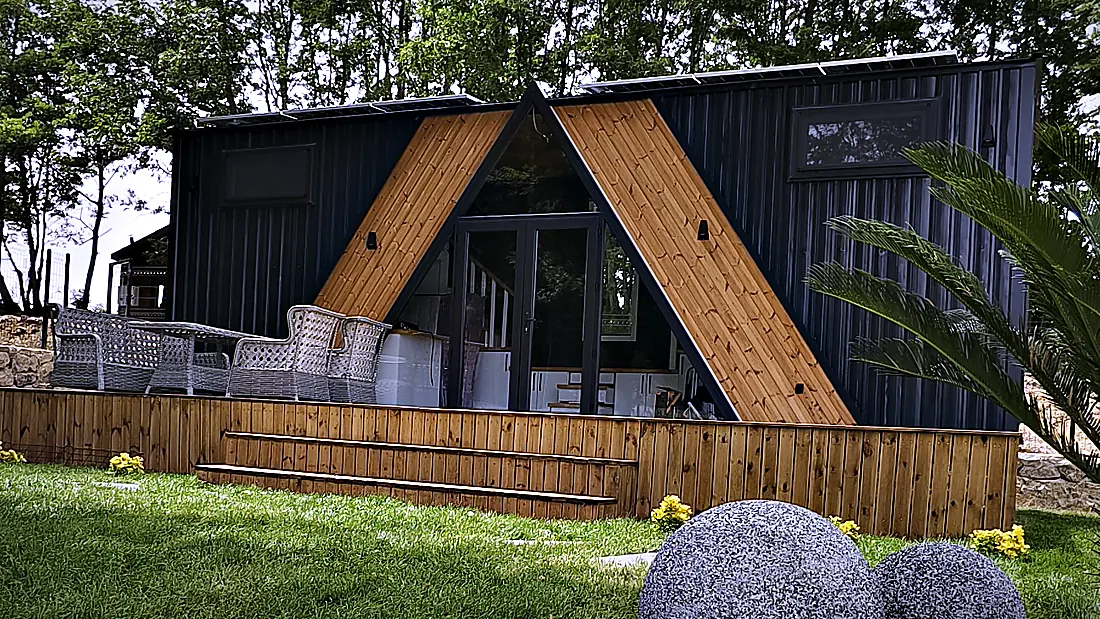 Tiny House mit A-Frame-Giebel und Holzfassade auf einer Rasenfläche, seitliche Ansicht