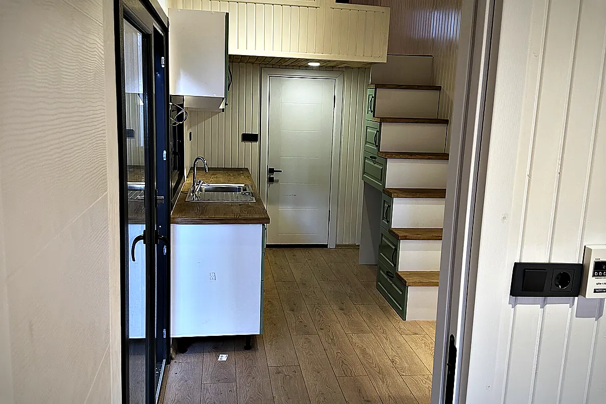 Blick durch eine geöffnete Tür in den Innenraum einer Einheit, Küchenblock und Treppe zum Loft