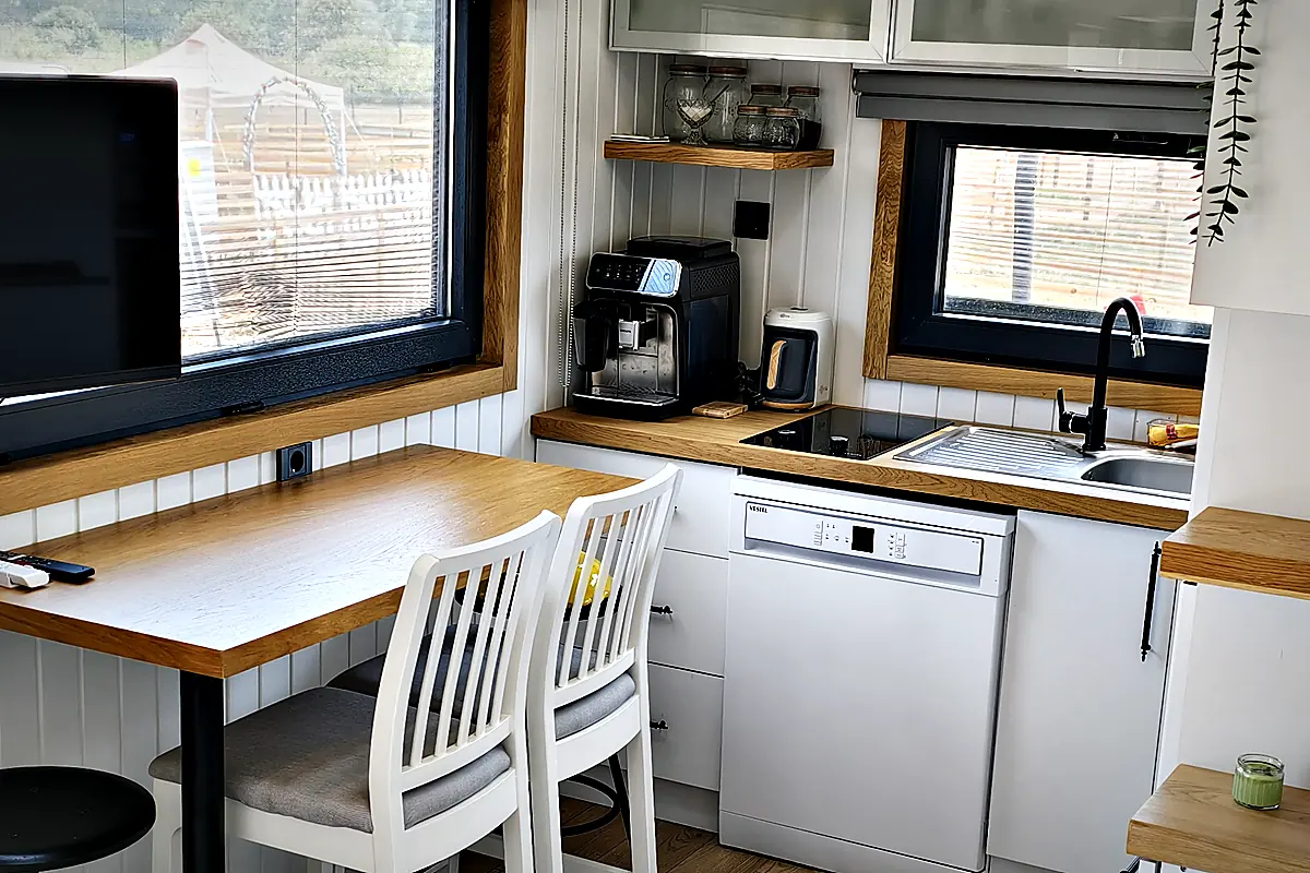 Innenraum eines Tiny House mit Küchenzeile, Esstisch am Fenster und Sitzbereich
