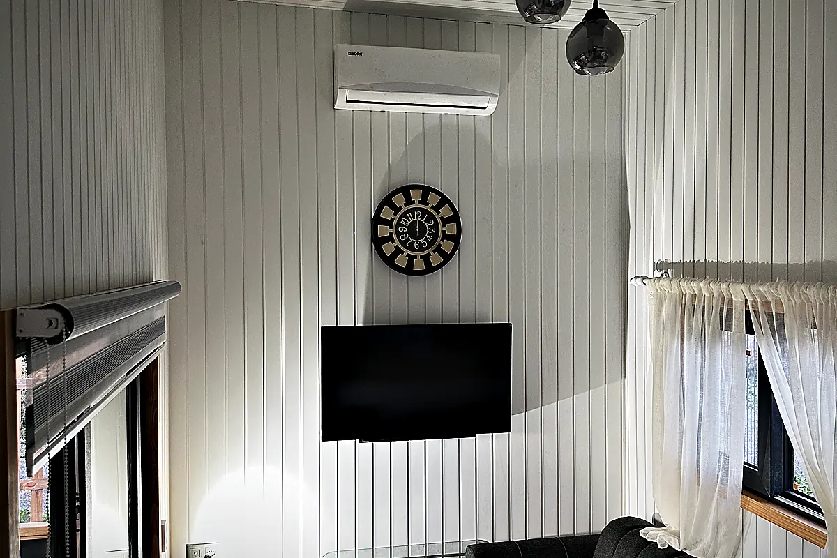 Wohnbereich mit Ecksofa, Wandfernseher, Pendelleuchten und weiss profilierter Wand- und Deckenverkleidung
