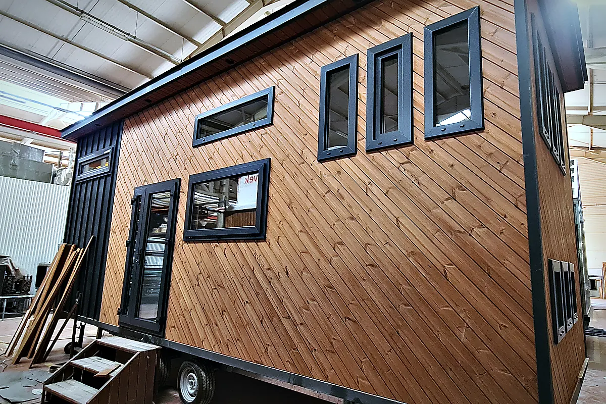 Tiny House in der Fertigung: Holzfassade montiert, Fenster eingesetzt, Modul auf dem Fahrgestell