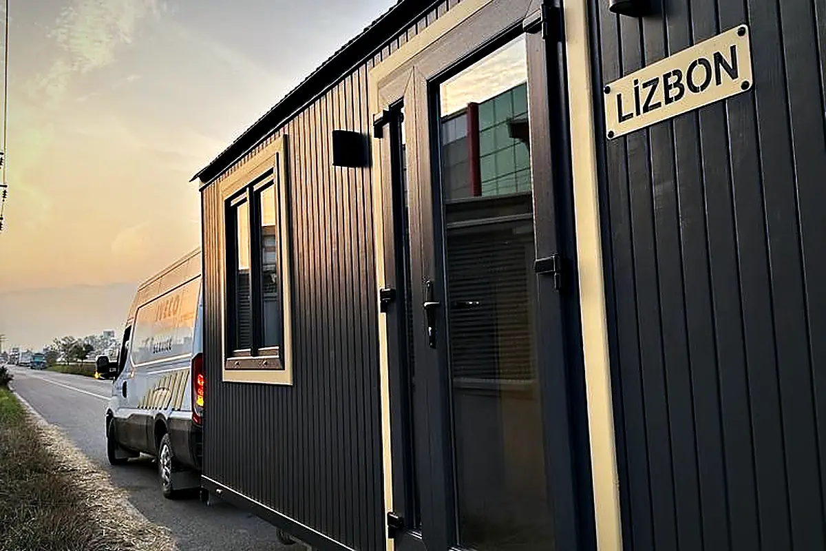 Tiny House auf dem Anhänger hinter dem Zugfahrzeug, unterwegs auf der Landstraße bei Abendlicht